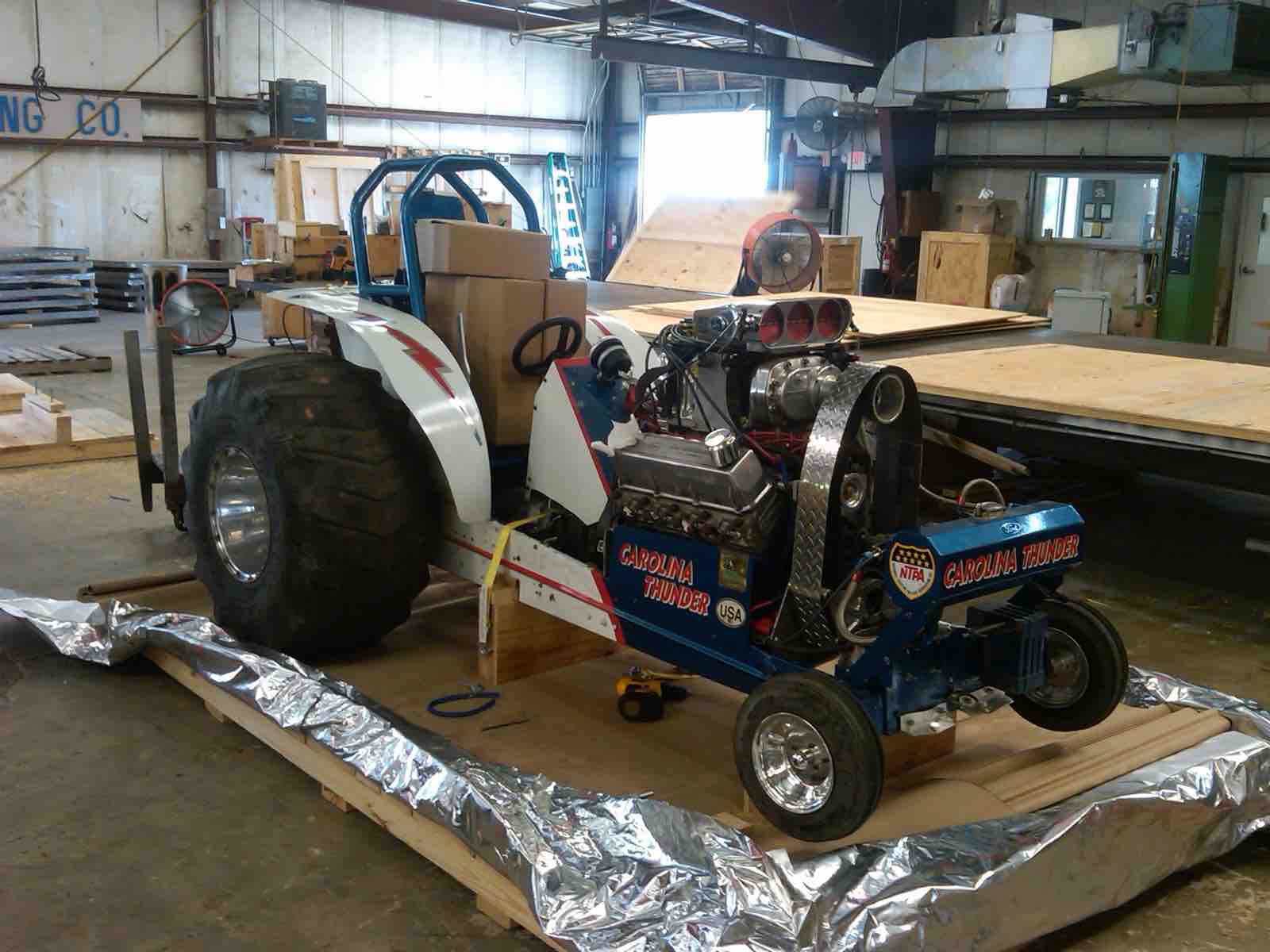 Racing tractor on a wooden crate base being wrapped in barrier foil