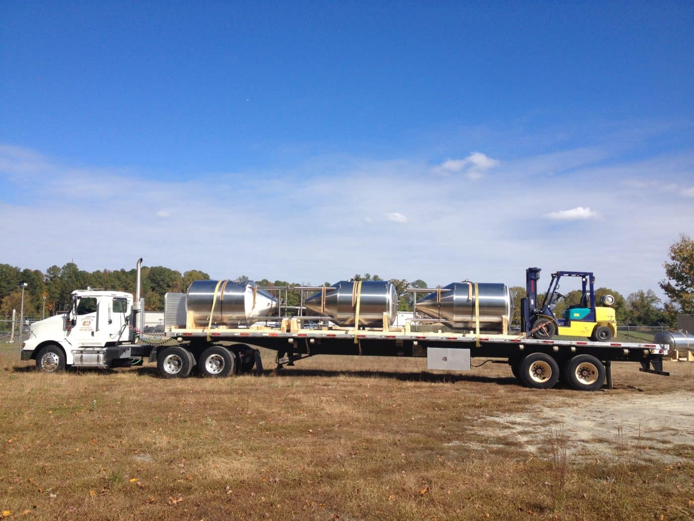 Steel tanks loaded on a flatbed truck beside a forklift