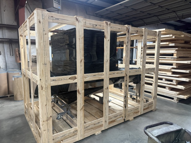 Shrink-wrapped machine inside a tall open wooden crate